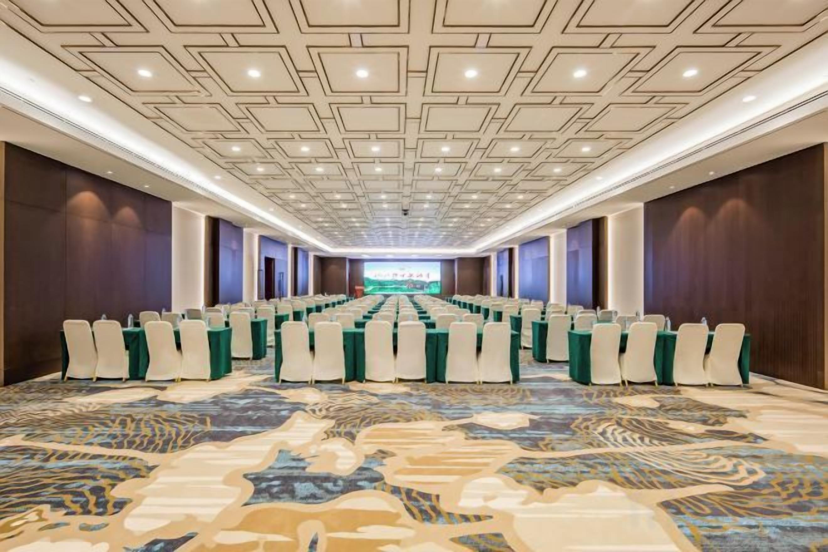 A conference room with rows of chairs, a stage, and a patterned carpet.