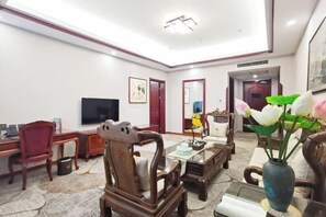 Un salón espacioso con techo alto, televisor, muebles de madera y un florero con flores.