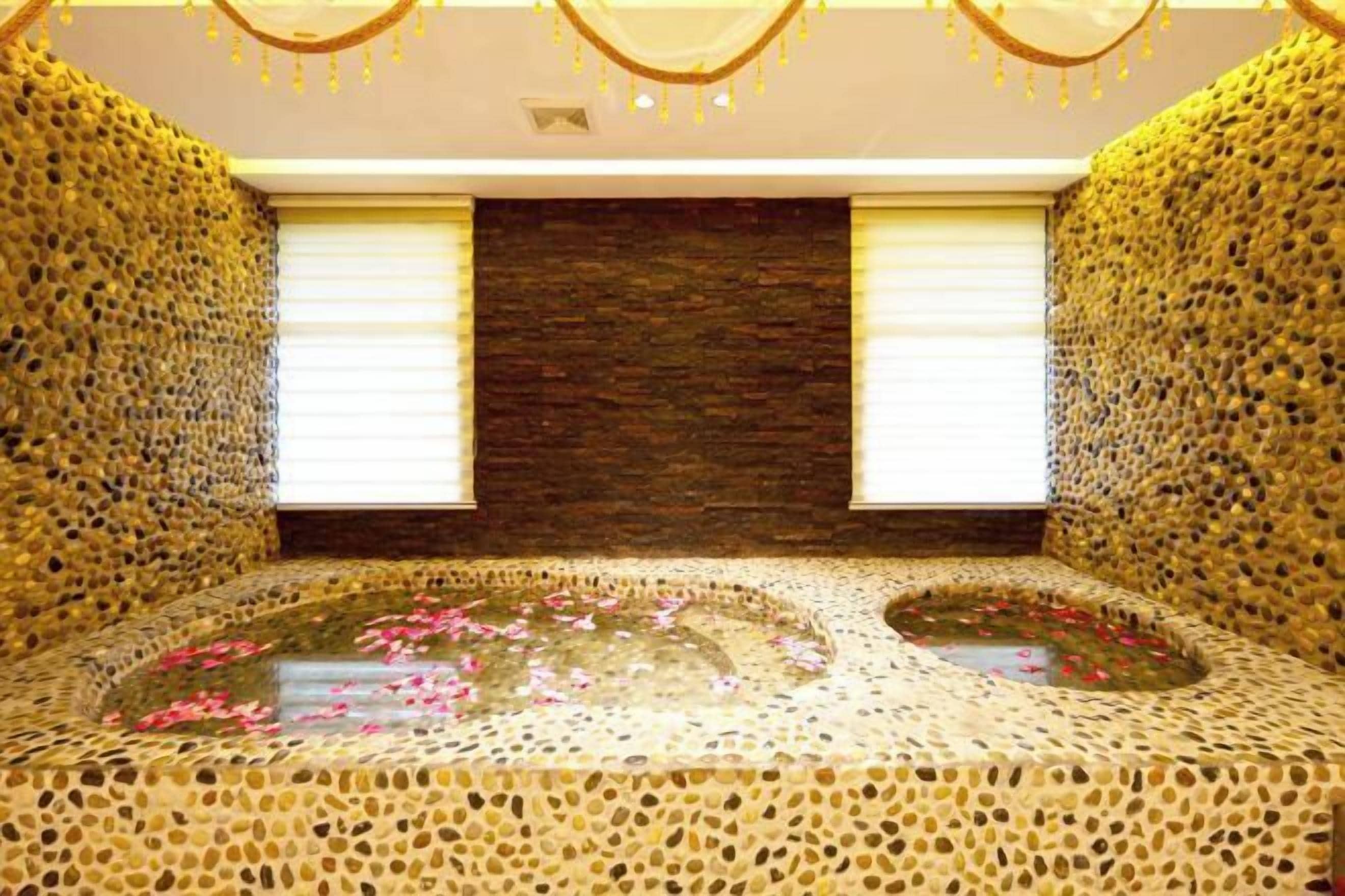 A spa room with a mosaic floor, a central water feature with rose petals, and a stone wall.