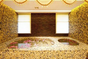 Un cuarto de spa con piso de mosaicos, un elemento central de agua con pétalos de rosa y una pared de piedra.