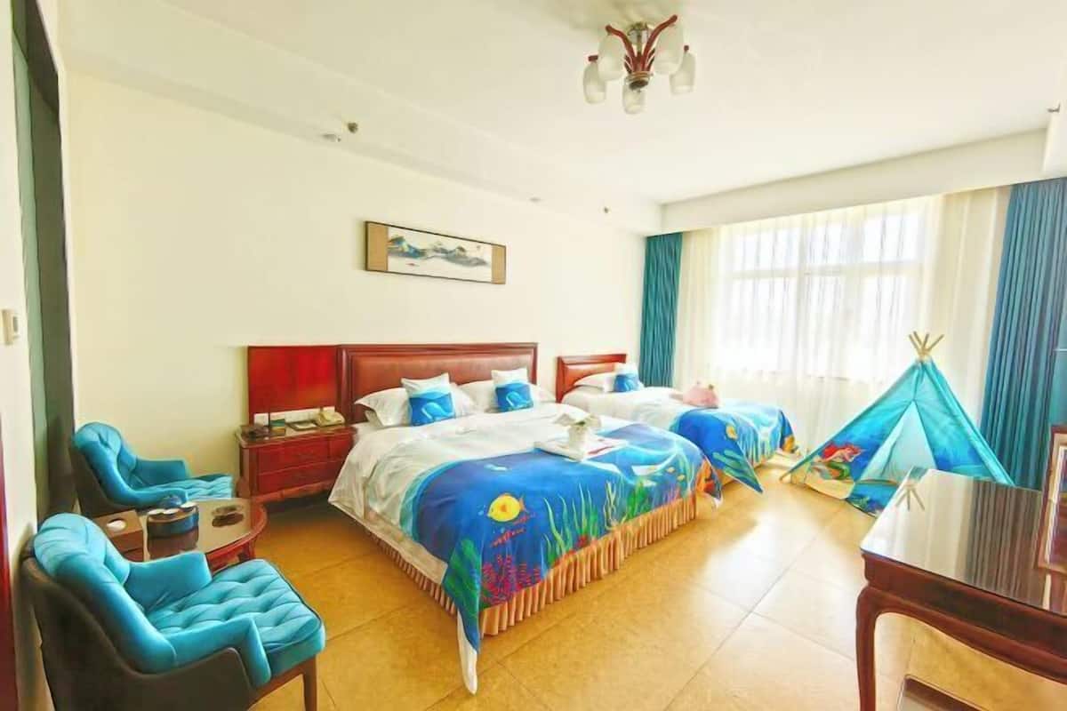 A hotel room with two beds, a desk, a chair, a window with curtains, and a painting on the wall.