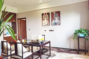 A modern living room with a dark wooden coffee table, two white cushioned chairs, a potted plant, and two framed artworks on the wall.