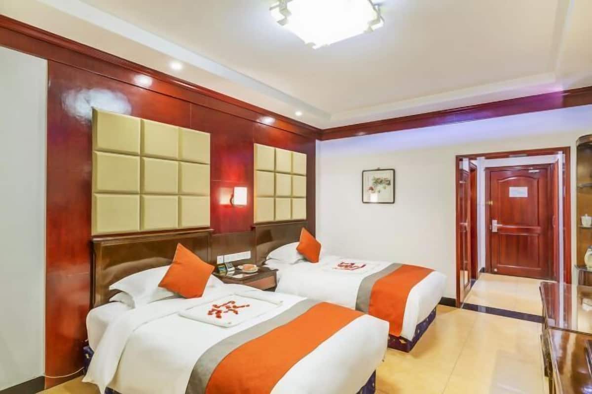 A hotel room with two beds, a wooden headboard, a nightstand, and a framed picture on the wall.