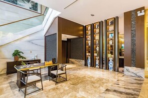 Et hotellobby med et marmorgulv, en trappe, en receptionsdisk og en reol.