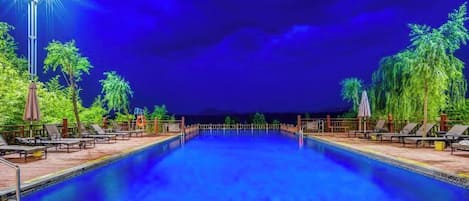 A swimming pool with lounge chairs and umbrellas, surrounded by palm trees.