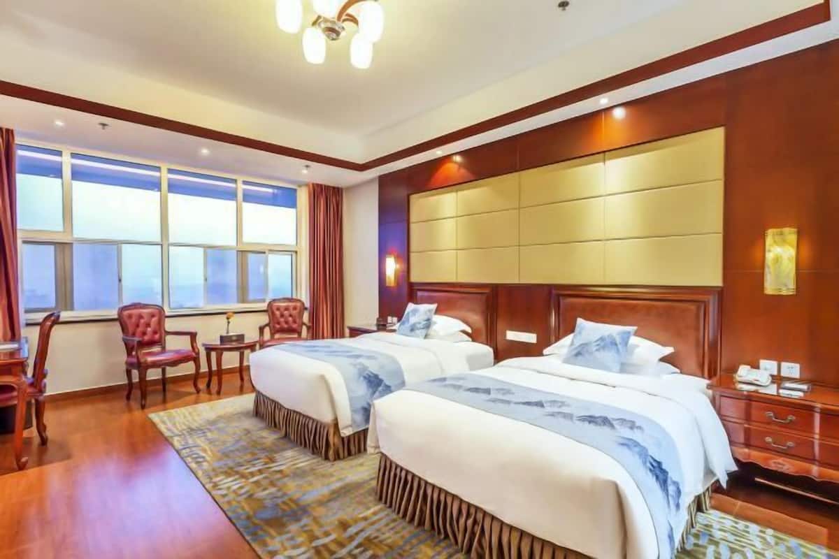 A hotel room with two beds, a large window, a wooden headboard, and a desk with a chair.