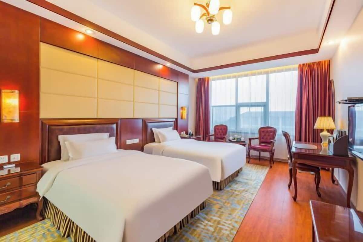 A hotel room with two beds, a desk, a chair, and a large window.