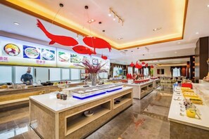 Un amplio vestíbulo de hotel con un mostrador de recepción central, varias zonas de estar y un techo bien iluminado decorado con adornos rojos colgantes.