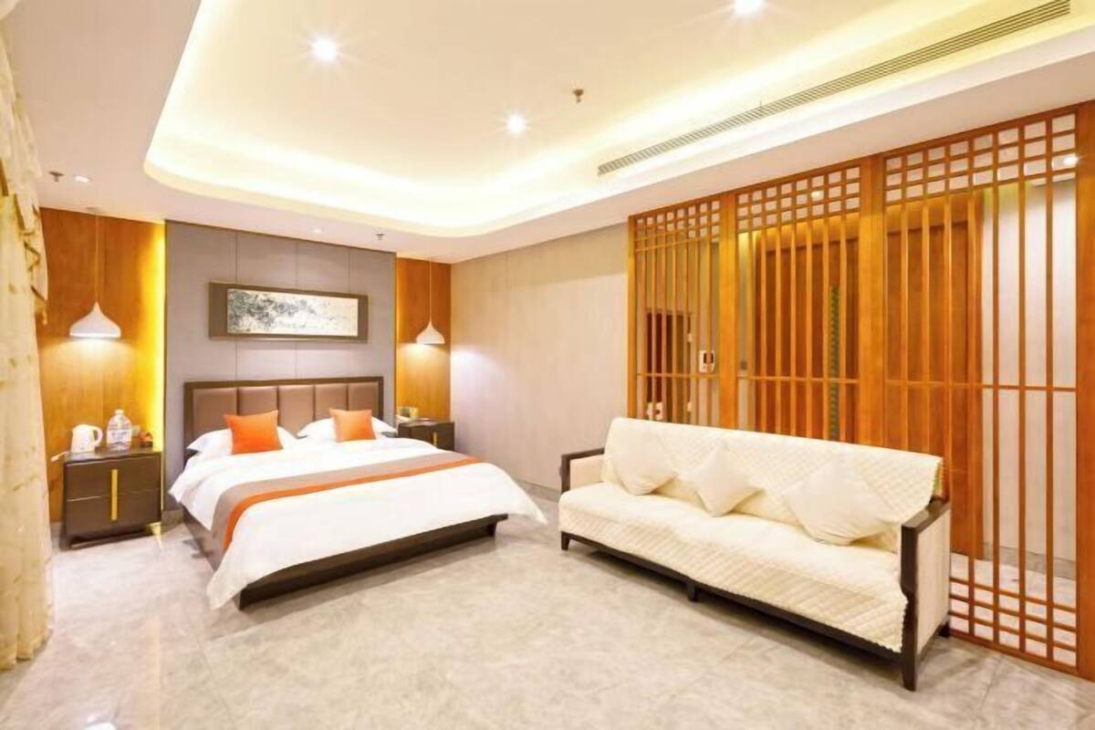 A hotel room with a bed, a sofa, a wooden partition, and a nightstand with a lamp.