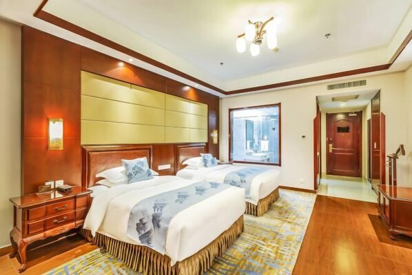 Habitación de hotel con dos camas, cabecero de madera, mesita de noche y un ventanal grande.