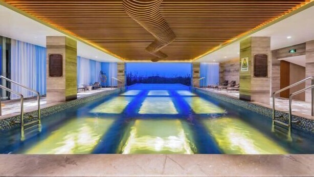 A large indoor swimming pool with a modern design, surrounded by lounge areas and a view of the night sky. - Hebei Yeshengyuan Hotel (Pingshan)