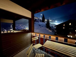 Ein Balkon mit Holzbanken und Blick auf eine verschneite Berglandschaft in der Nacht.