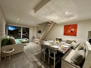 A modern living room with a dining area, a staircase, and a large window. - New! Beautiful "ski-in, ski-out" duplex apartment in the center of La Clusaz (La Clusaz)