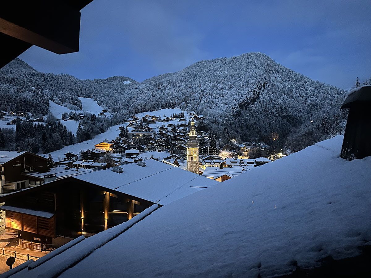 A snow-covered village with traditional wooden houses and a prominent church tower.