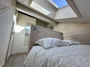 Une chambre avec un puits de lumière, une tête de lit en bois et un lit recouvert de linge de lit blanc.
