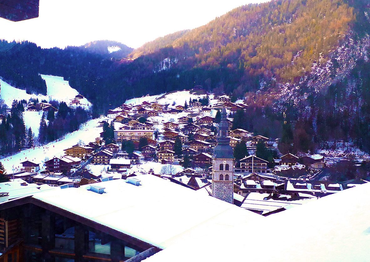 A snow-covered village with traditional wooden buildings and a prominent church tower.