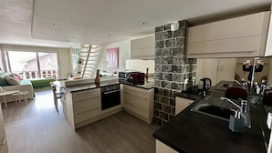 A modern kitchen with a central island, built-in appliances, and a stone accent wall. - New! Beautiful duplex "ski in ski out" La Clusaz center  (La Clusaz)
