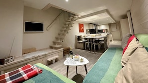 A modern living room with a sofa, a coffee table, and a staircase leading to a kitchen area. - New! Beautiful duplex "ski in ski out" La Clusaz center  (La Clusaz)