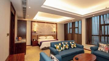 A modern hotel room with a large bed, a sitting area with a sofa and armchairs, and a small table.