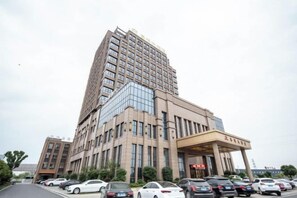 A multi-story hotel with a prominent entrance, a parking lot with several cars, and a clear sky. - Jiade Hotel (Tongxiang)