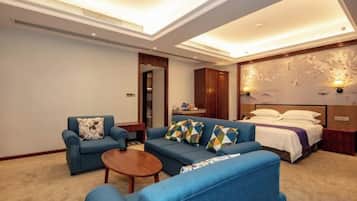 A hotel room with a sofa, a small table, a bed, and a wall-mounted TV.