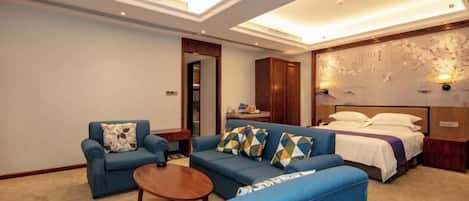 A hotel room with a sofa, a small table, a bed, and a wall-mounted TV.