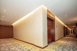 A hotel hallway with a reception desk, a wooden door, and a carpeted floor. - Jiade Hotel (Tongxiang)