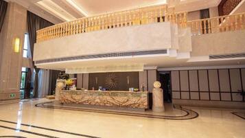 A spacious lobby with a marble reception desk, a second-floor balcony, and a modern ceiling design.