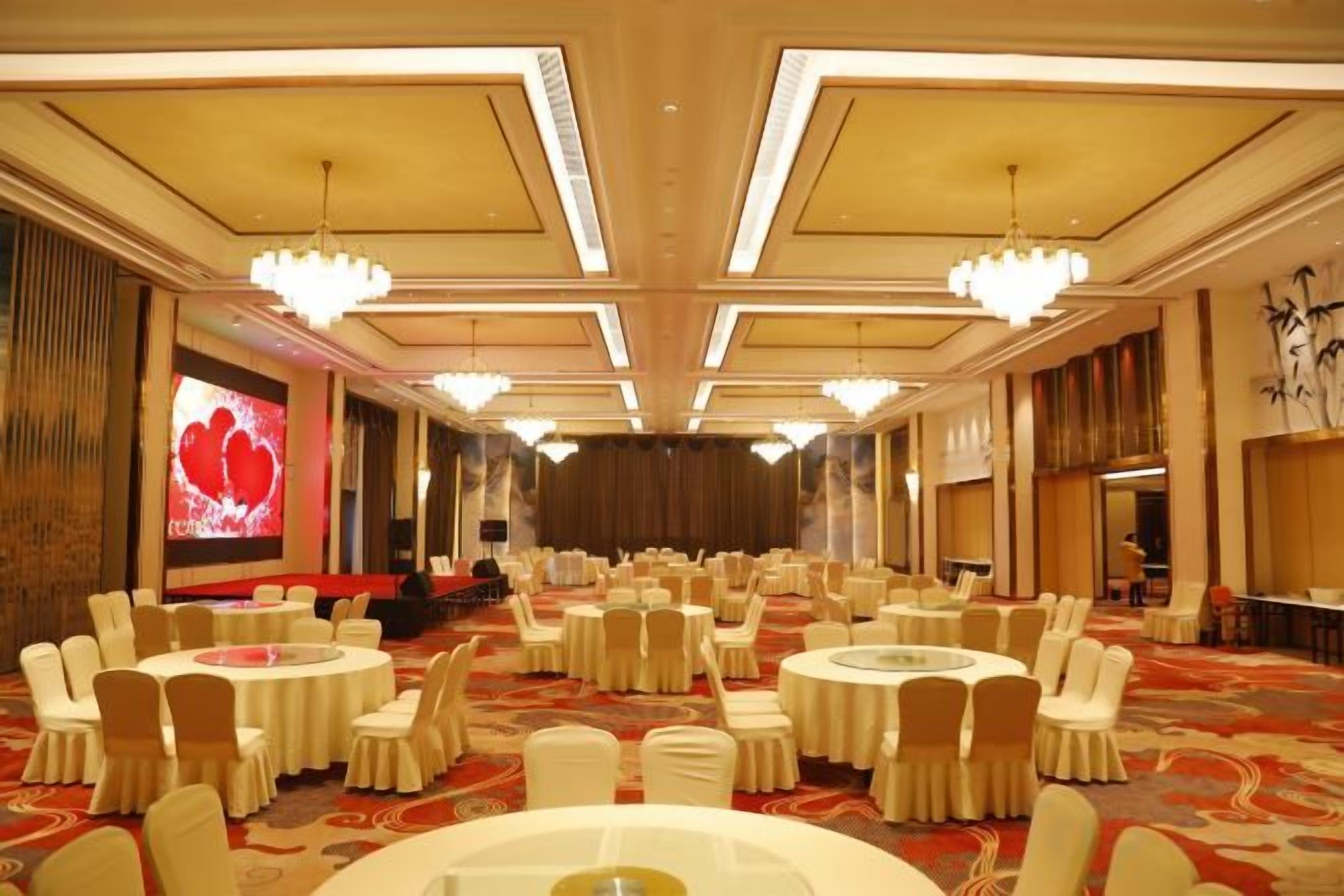 A banquet hall with round tables and chairs, a stage, and a large screen.