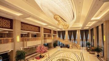 A spacious lobby with a grand staircase, decorative ceiling, and a central fountain.