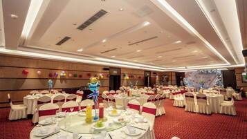 A banquet hall with round tables, white tablecloths, and red carpet flooring.