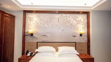 A hotel room with a large bed, wooden headboard, two bedside tables with lamps, and a decorative wall piece above the bed.