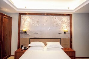 Habitación de hotel con una cama grande, cabecera de madera, dos mesitas de noche con lámparas y un adorno decorativo sobre la cama.
