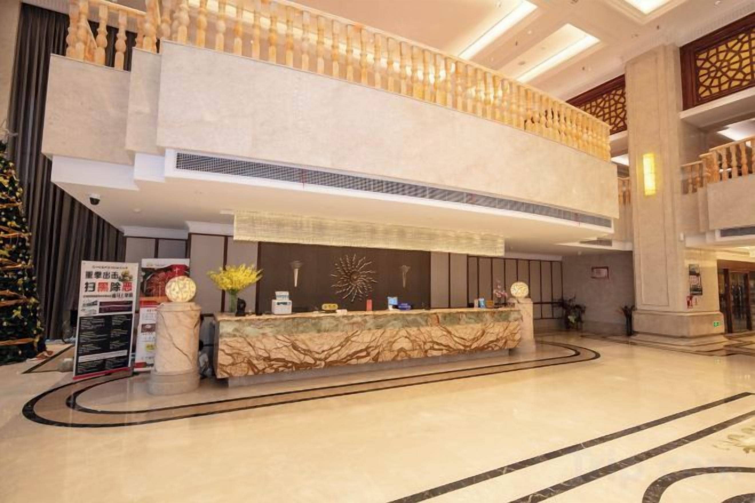 A hotel lobby with a reception desk, a Christmas tree, and a high ceiling with decorative lighting.