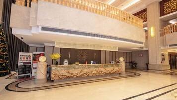 A hotel lobby with a reception desk, a Christmas tree, and a high ceiling with decorative lighting.
