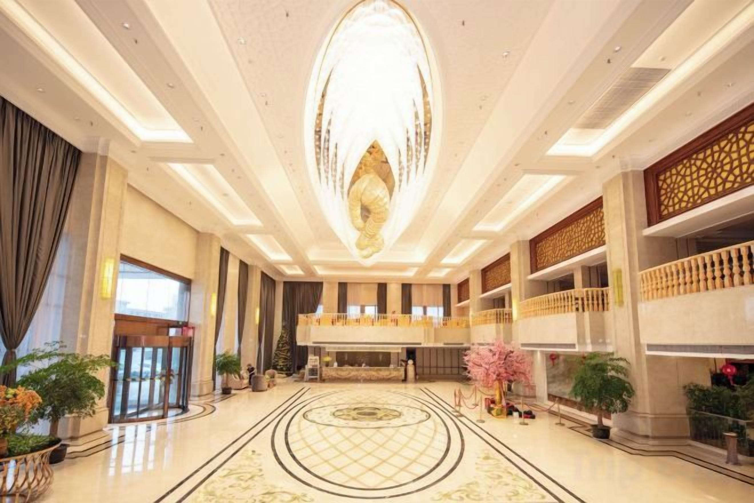 A spacious lobby with a grand chandelier, a reception desk, and a decorative floor pattern.