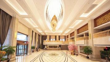 A spacious lobby with a grand chandelier, a reception desk, and a decorative floor pattern.