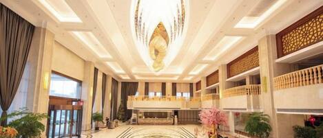 A spacious lobby with a grand chandelier, a reception desk, and a decorative floor pattern.