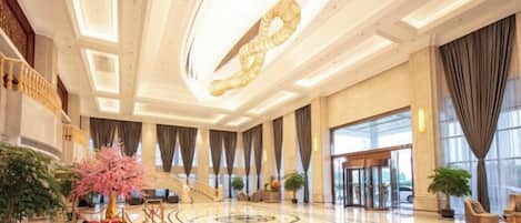 A spacious lobby with a grand staircase, a large chandelier, and a central decorative tree.