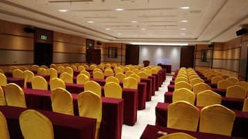 A conference room with rows of tables and chairs, equipped with a podium and a projection screen.