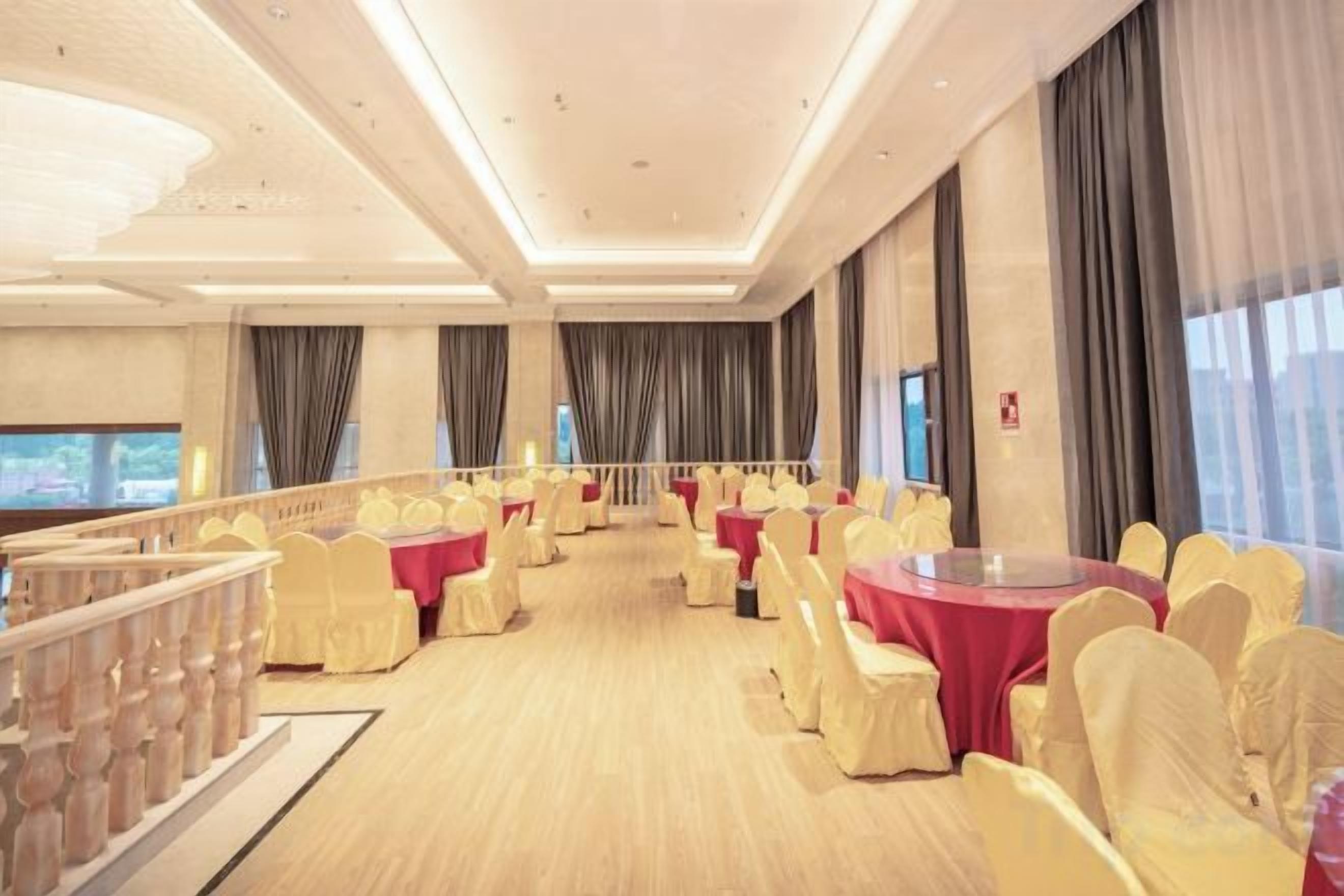 A banquet hall with round tables and chairs, a balcony, and a large window.