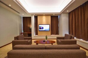 A hotel room with a large flat-screen TV mounted on the wall, two sofas, a small coffee table, and a potted plant. - Jiade Hotel (Tongxiang)