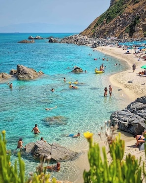 Une plage avec une eau turquoise et limpide, des formations rocheuses et des gens qui se baignent et prennent des bains de soleil.