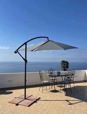 A patio with a table and chairs, a large umbrella, and a view of the ocean.