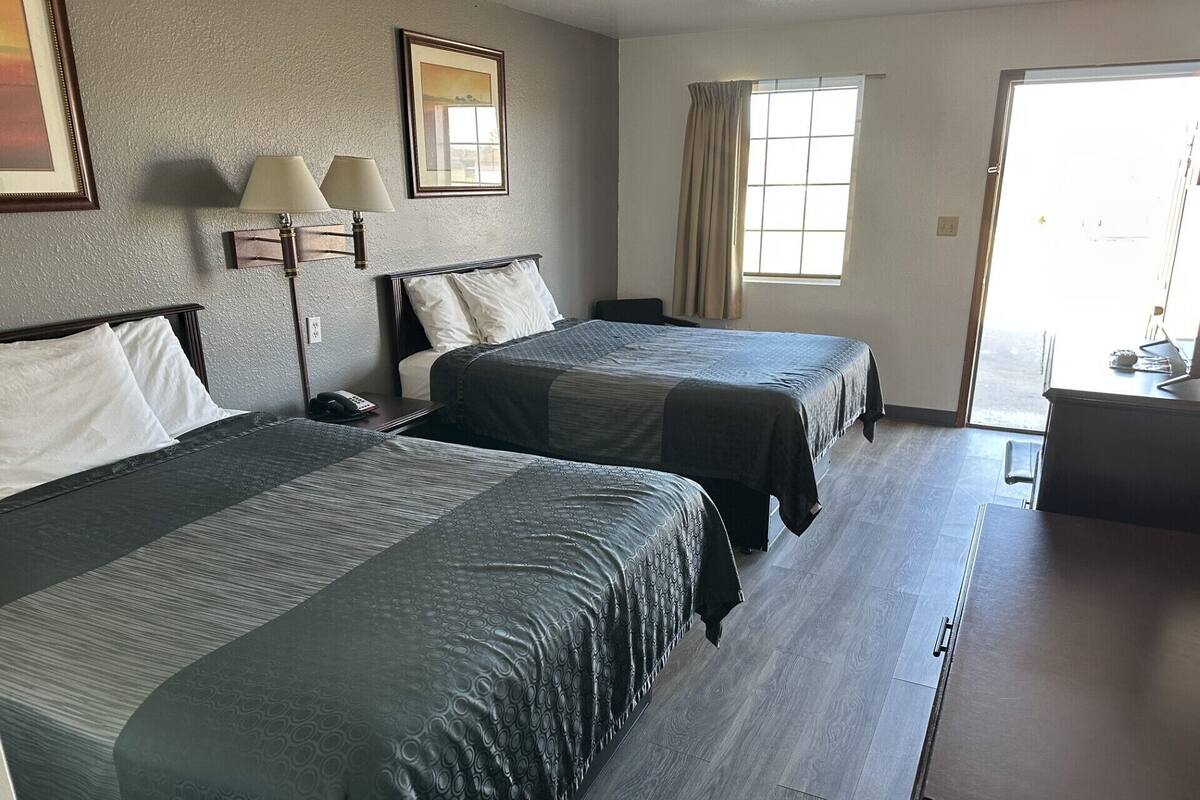 A hotel room with two beds, a desk, a lamp, and a window with curtains.