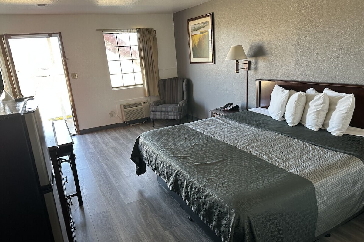 A hotel room with a large bed, a chair, a desk, a lamp, and a window.