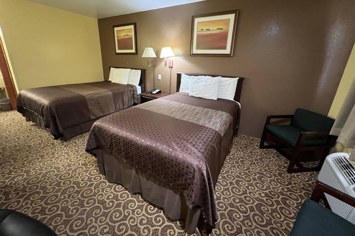 A hotel room with two beds, a desk, a chair, a lamp, and a picture on the wall.