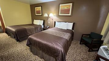 A hotel room with two beds, a desk, a chair, a lamp, and a picture on the wall.