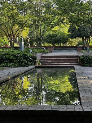 A tranquil garden with a rectangular pond, stone steps leading up to a brick wall, and lush greenery.