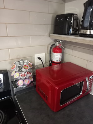 Uma cozinha com micro-ondas vermelho, cafeteira e extintor de incêndio.